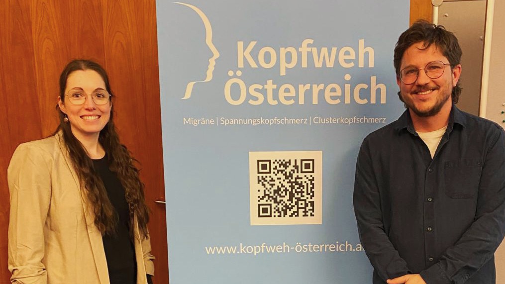 David Sonntagbauer und eine Vertreterin von Kopfweh Österreich vor dem Vereinsbanner in Linz
